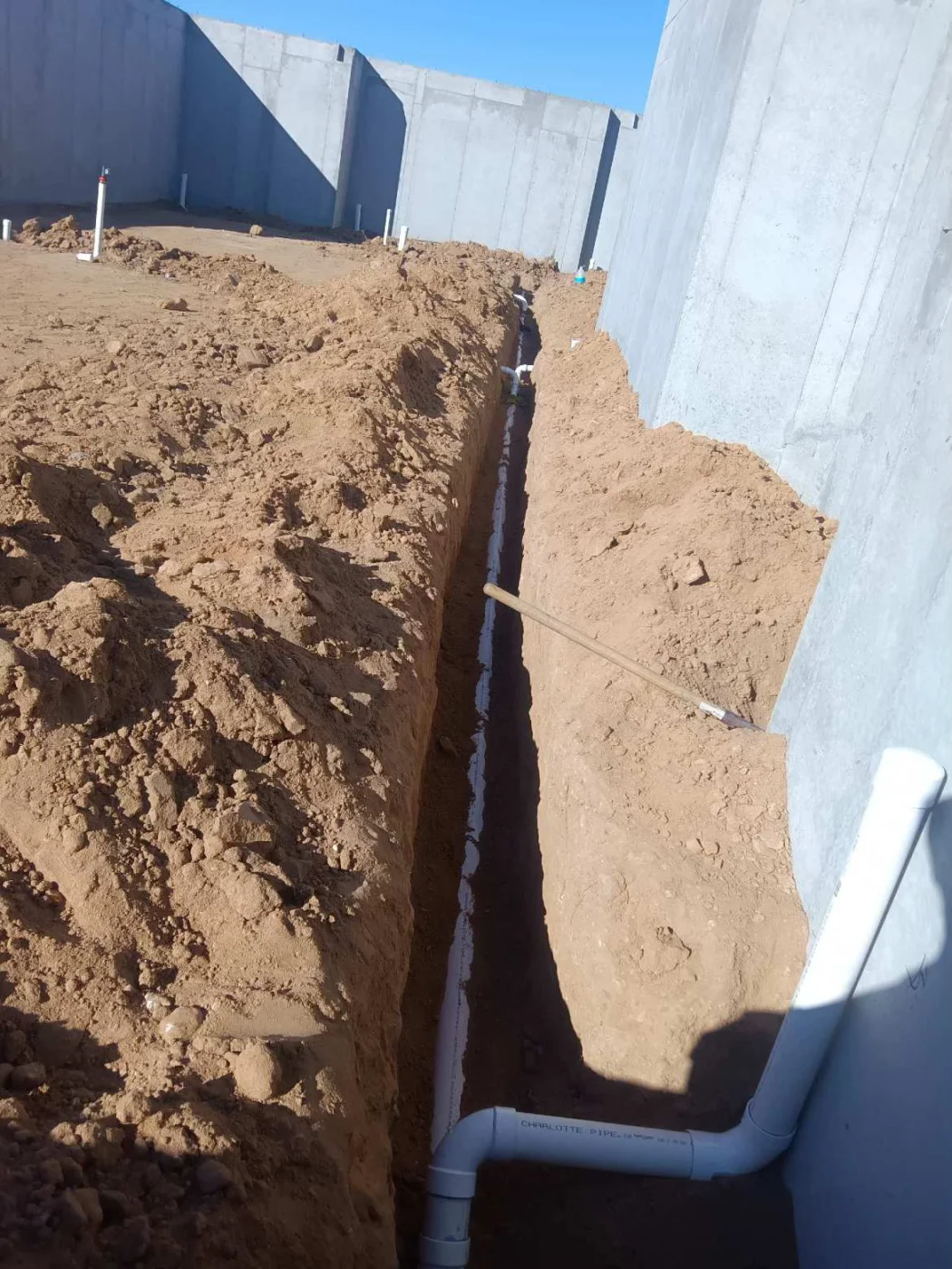 Exterior trench with new underground piping installed beside a foundation wall