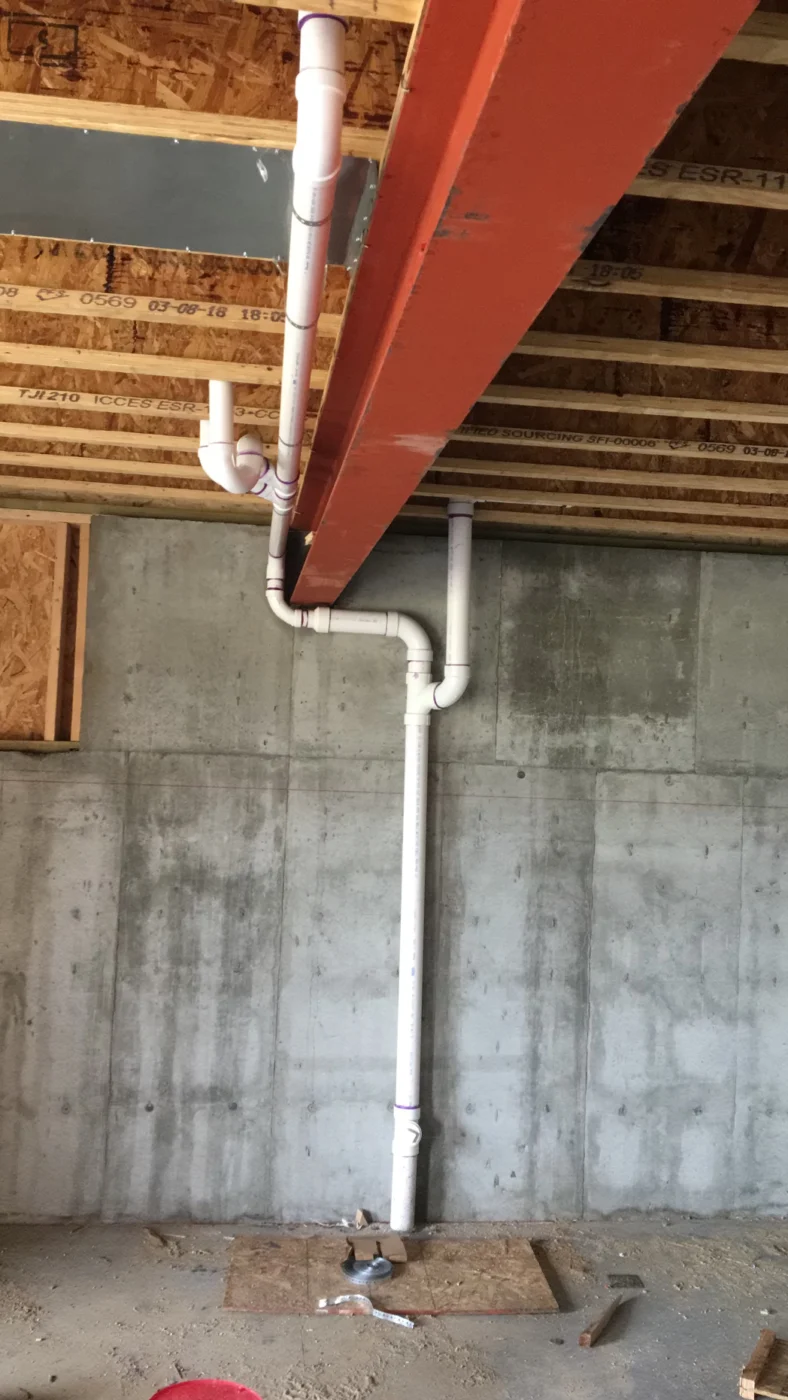 Vertical drain pipe and basement plumbing installed near a foundation wall